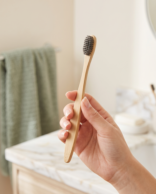 Person holding a bamboo toothbrush in a bright bathroom